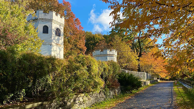 A pathway stretching past two castle-like structures at ​Snug Harbor Cultural Center & Botanical Garden as leaves start to change color on Staten Island