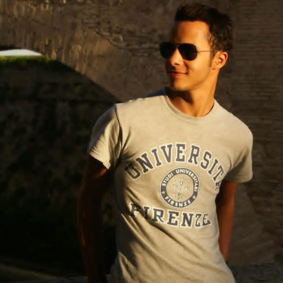person wearing a universitythemed shirt and red pants near a stone structure
