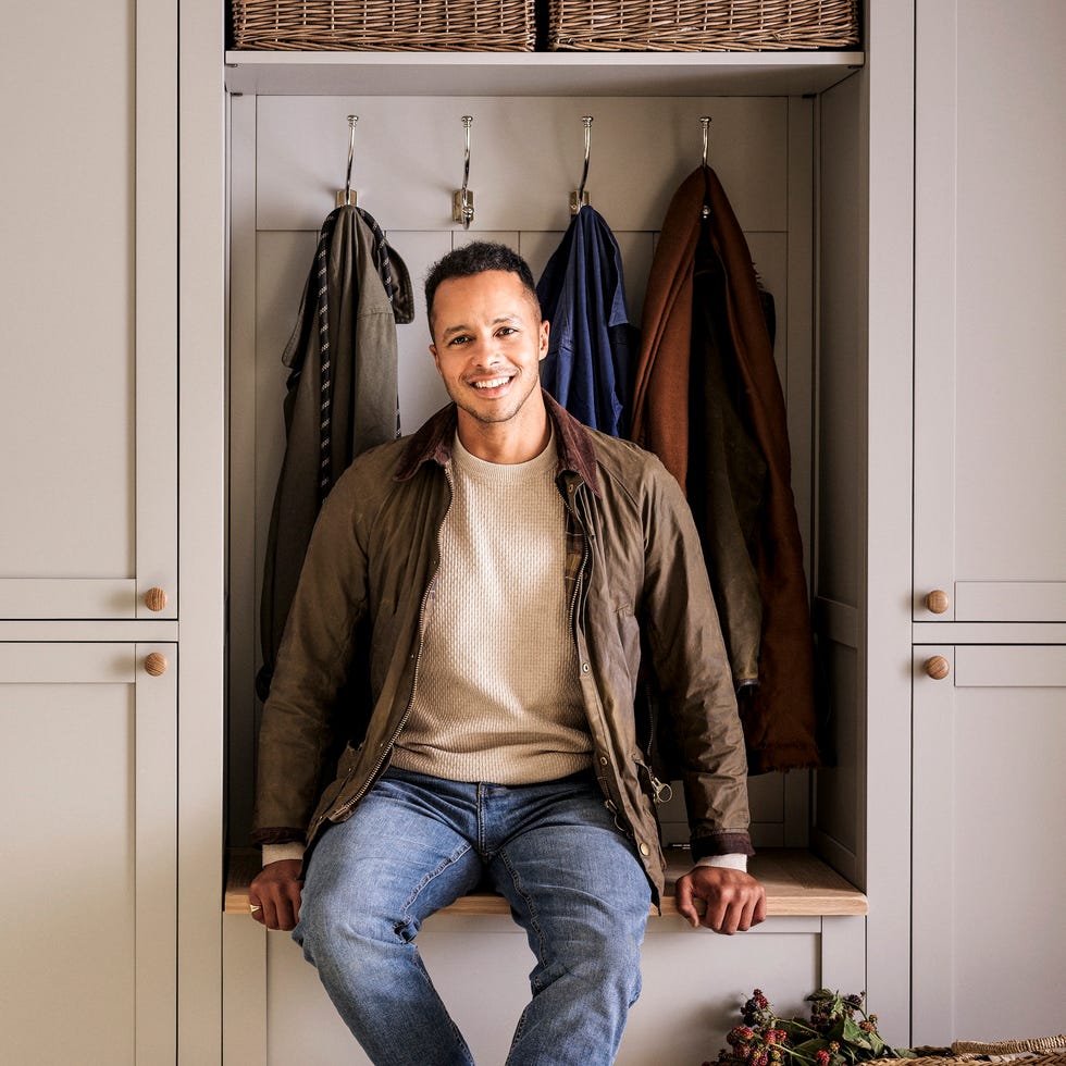 mudroom with a person seated on a storage bench surrounded by coats and organizational items