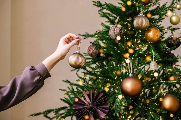 Young woman's hand decorating Christmas tree indoors. Close up.
