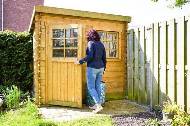 Woman opening the door of a wooden shed in her backyard garden