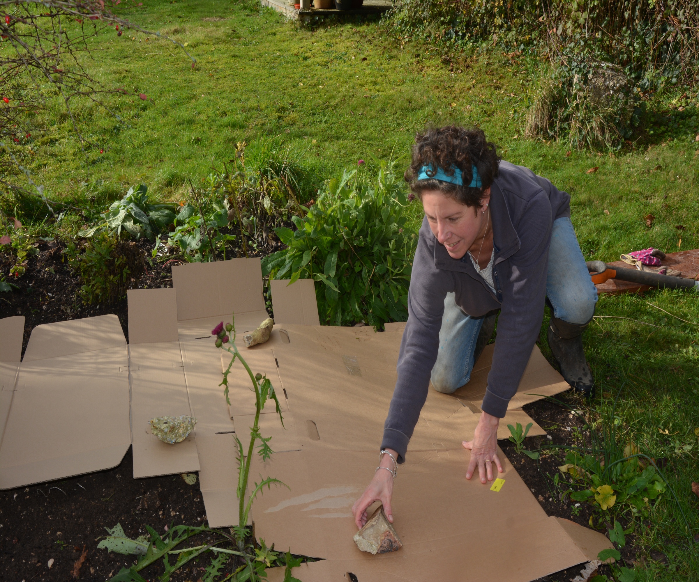 Flattened cardboard covering bare oil, with a woman securing it using a large stone