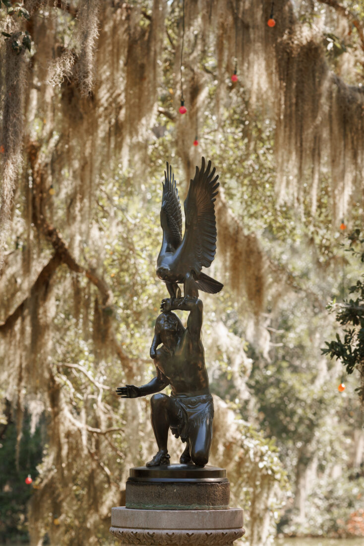 A sculpture of a person holding an eagle against a background of Spanish moss