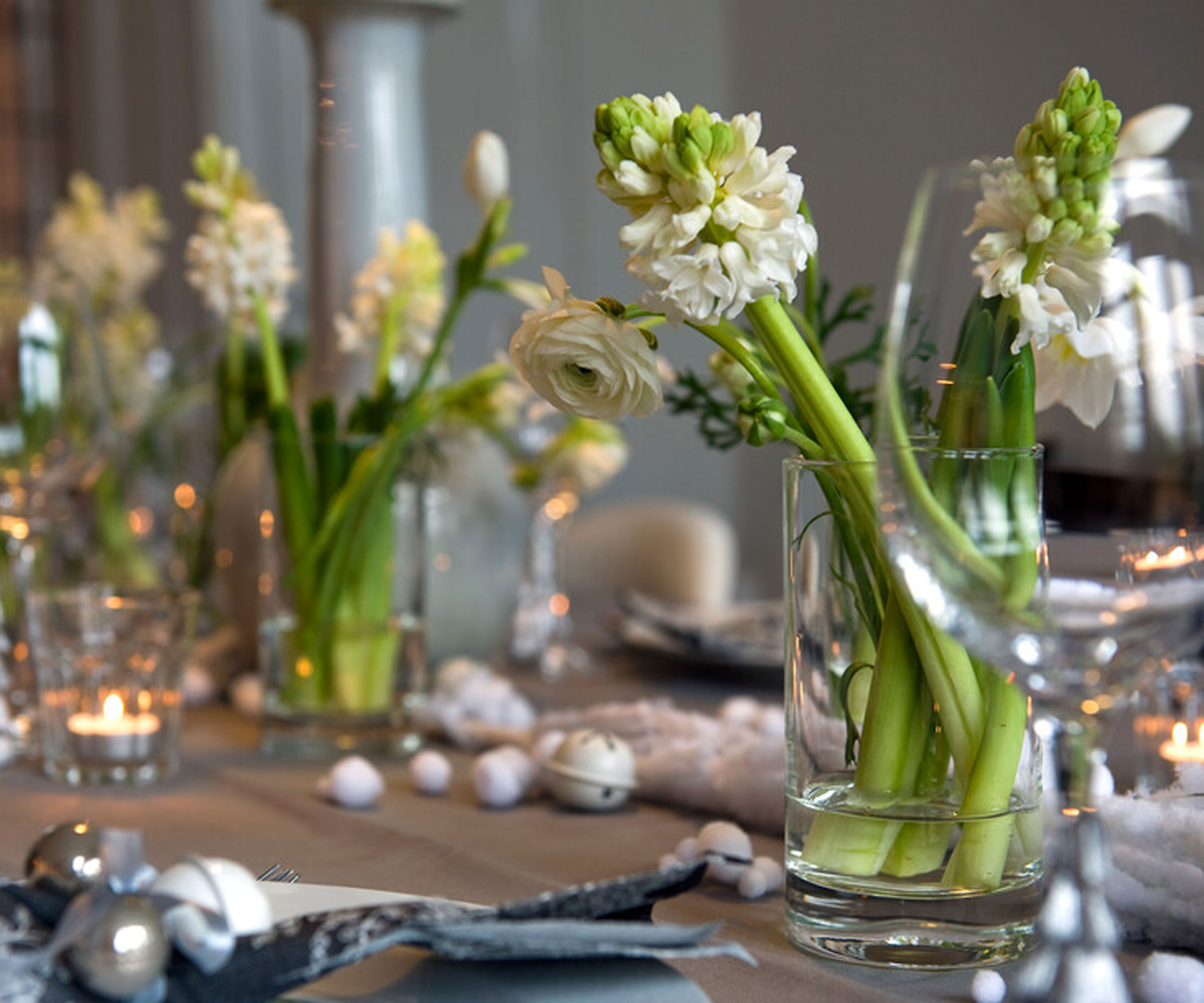 white hyacinths arranged in glass vases for christmas table decoration, with candles in glass jars and other christmas decorations like baubles