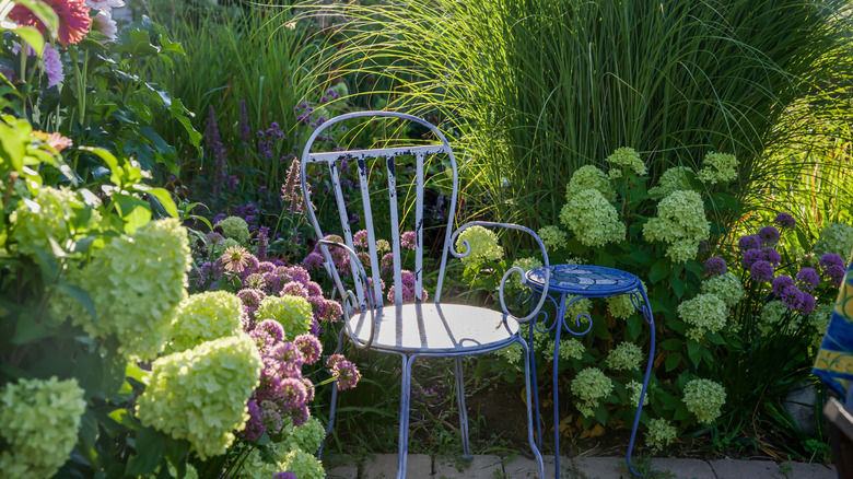 An antiqued metal and glass bistro set tucked away among hydrangea shrubs and tall grasses.