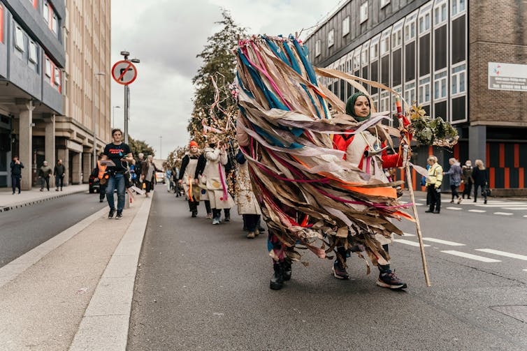 Women carry a silver birch tree through a city street.