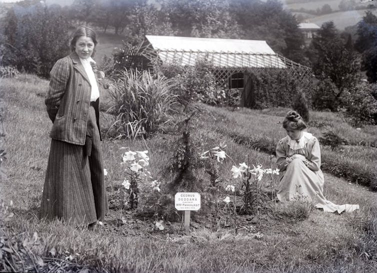 Two women stand by a newly planted tree in the garden of their retreat.