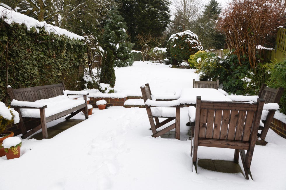 Winter patio and garden suburban snow covered patio with garden furniture, garden in the background