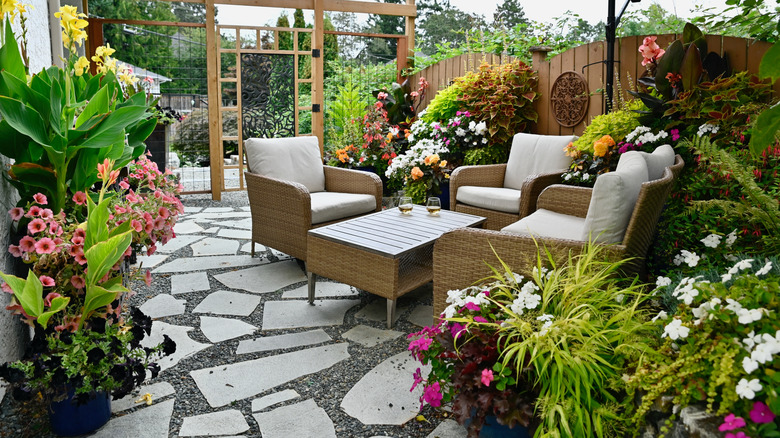 A backyard featuring a stone patio with lots of colorful flowering plants