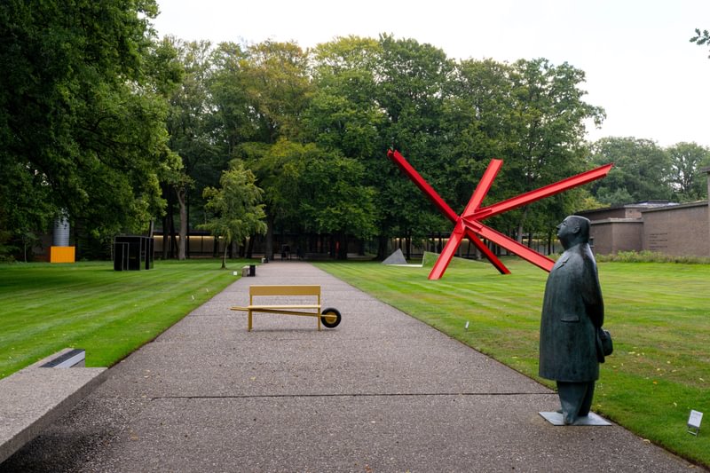 ochre yellow coats wheelbench’s rounded aluminum form in netherlands museum garden