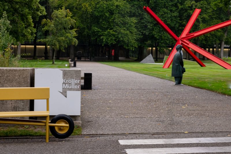 ochre yellow coats wheelbench’s rounded aluminum form in netherlands museum garden