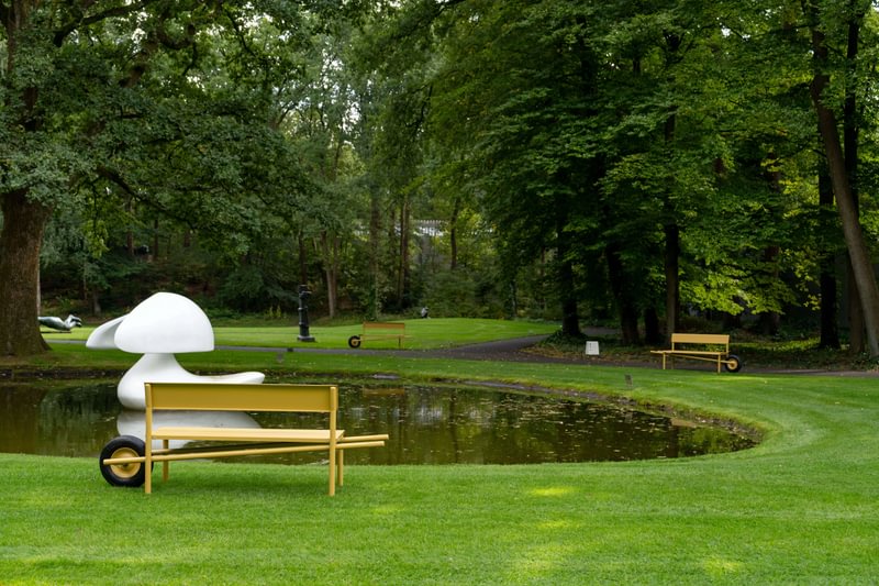 ochre yellow coats wheelbench’s rounded aluminum form in netherlands museum garden
