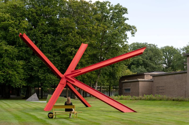 ochre yellow coats wheelbench’s rounded aluminum form in netherlands museum garden