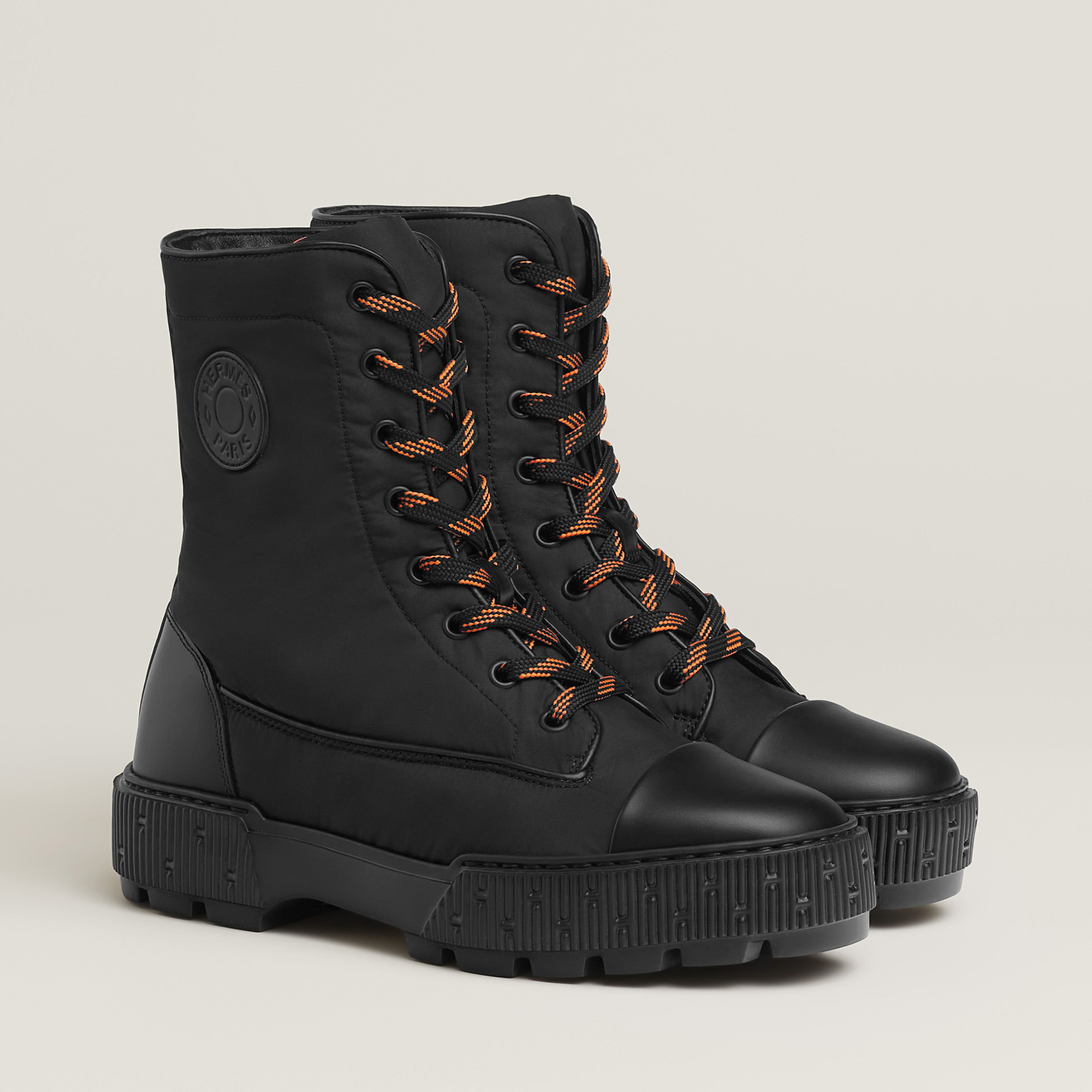Pair of black Hermes Fresh Ankle Boots with orange and black laces, and a circular Hermes logo on the side.