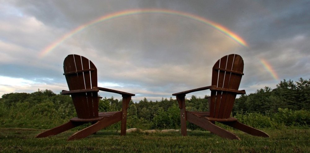 FILE - With two empty Adirondack chairs next to a fire pit, a rainbow stretches across the sky at Adams Pond in East Derry, N.H., Thursday July 1, 2010. (AP Photo/Charles Krupa, File)