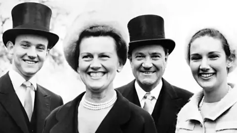 Mirrorpix Muriel and Alick McKay pictured in a group with two younger adults, possibly two of their children. They are smartly dressed with the men in top hats and Muriel and the other woman wearing white fur hats and pearl necklaces.