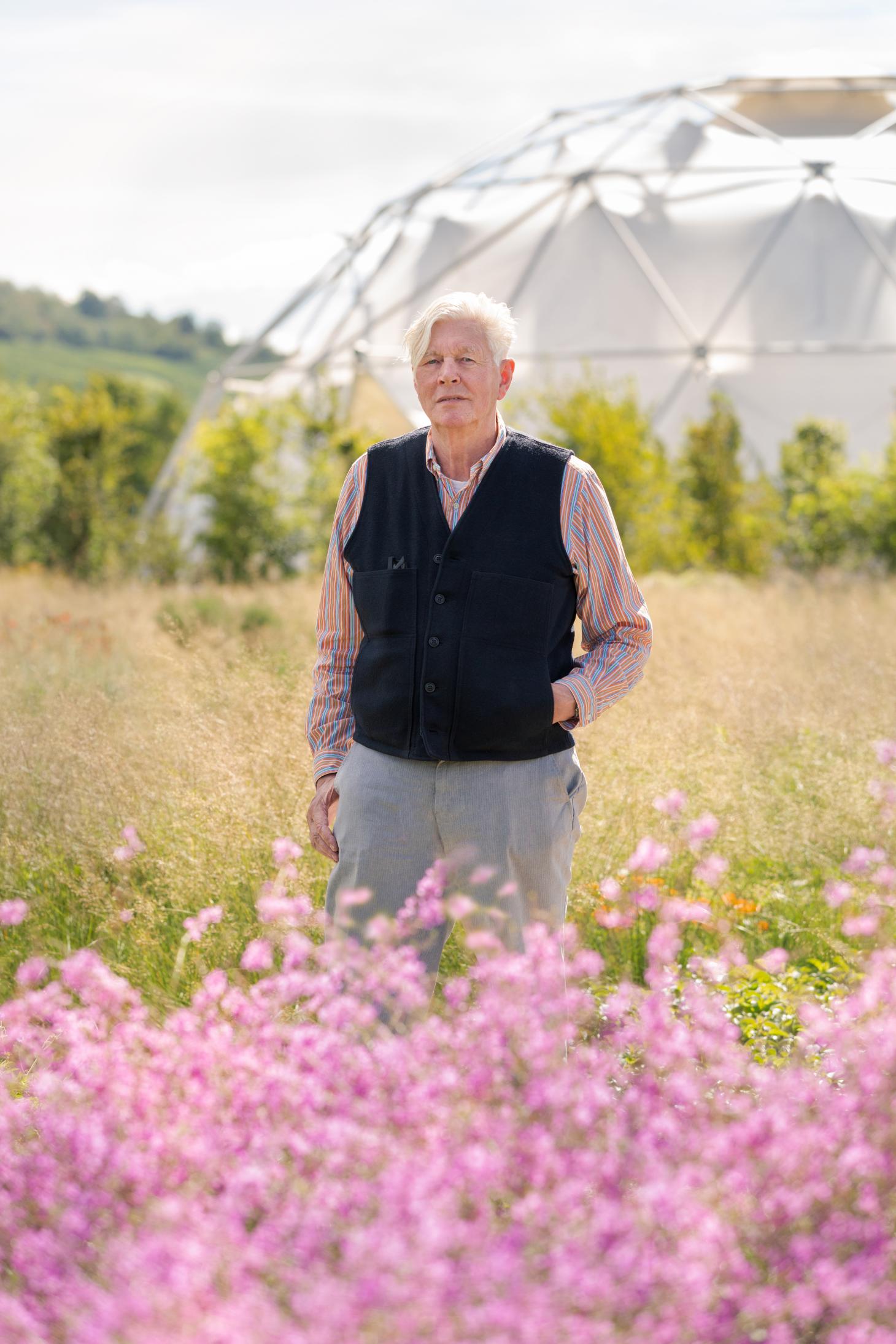 Dutch garden designer Piet Oudolf photographed among purple flowers in the garden he designed for Vitra in Weil am Rhein. Buckminster Fuller's dome is visible in the background