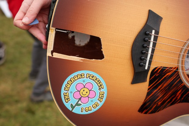 Joselyn Walsh holds her guitar on Oct. 10, 2025, near a hole she said was caused by federal agents shooting pepper balls and baton rounds at musicians, protesters and media near the U.S. Immigration and Customs Enforcement holding facility in Broadview. (Stacey Wescott/Chicago Tribune)