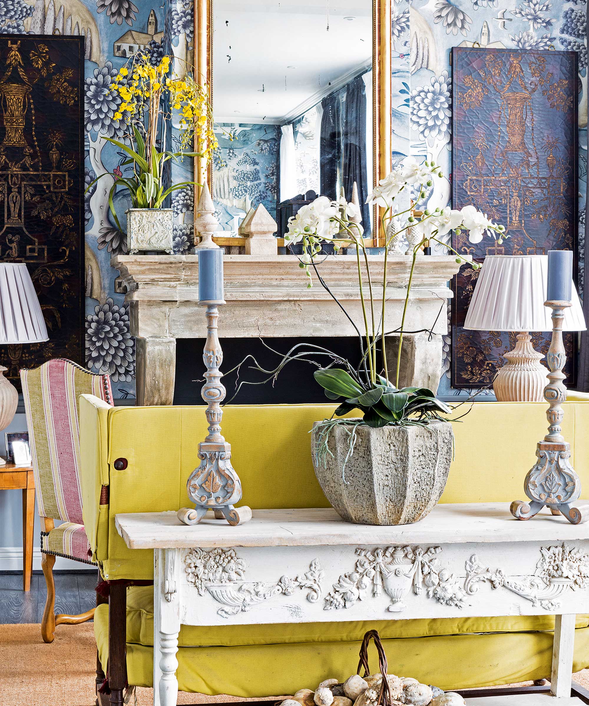 White orchid on a side table in front of yellow couch. The living room has blue patterned wallpaper.