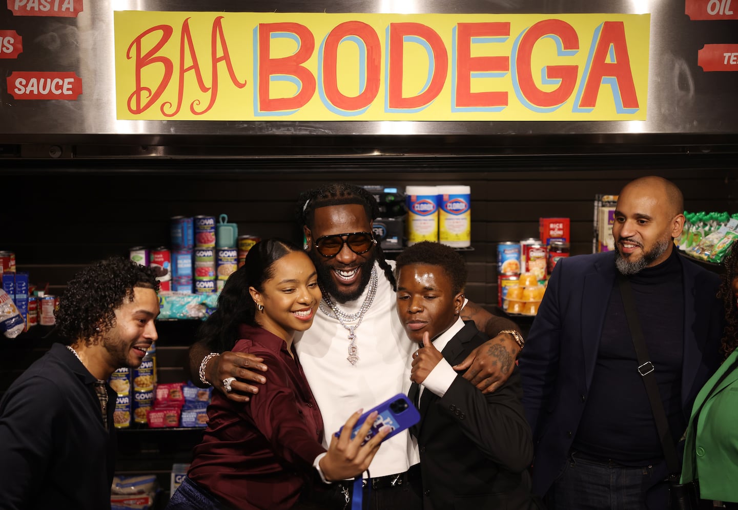 Nigerian musician Burna Boy (center) poses for a selfie with Edily Perez (left) and James Brice (right), members of the Boston Arts Academy who helped open the bodega and organize Burna Boy's appearance at Boston Arts Academy.