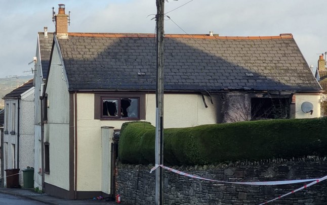 Pictured is the house in Caerphilly, Wales, where two people died after a garden explosion sparked a house fire on December 12, 2025. The windows are smashed and there is smoke damage to the property.