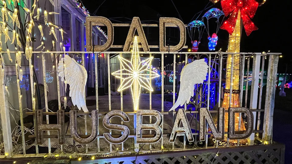 A metal sign that reads DAD HUSBAND with two angel wings, a star in the centre and strings of lights.