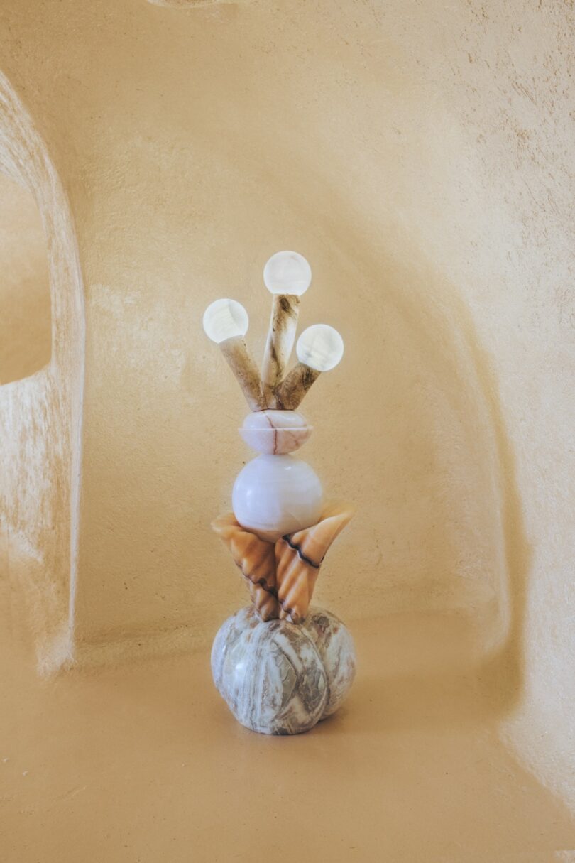 A sculptural arrangement of shells, stones, and horn-like objects stacked vertically against a textured beige background