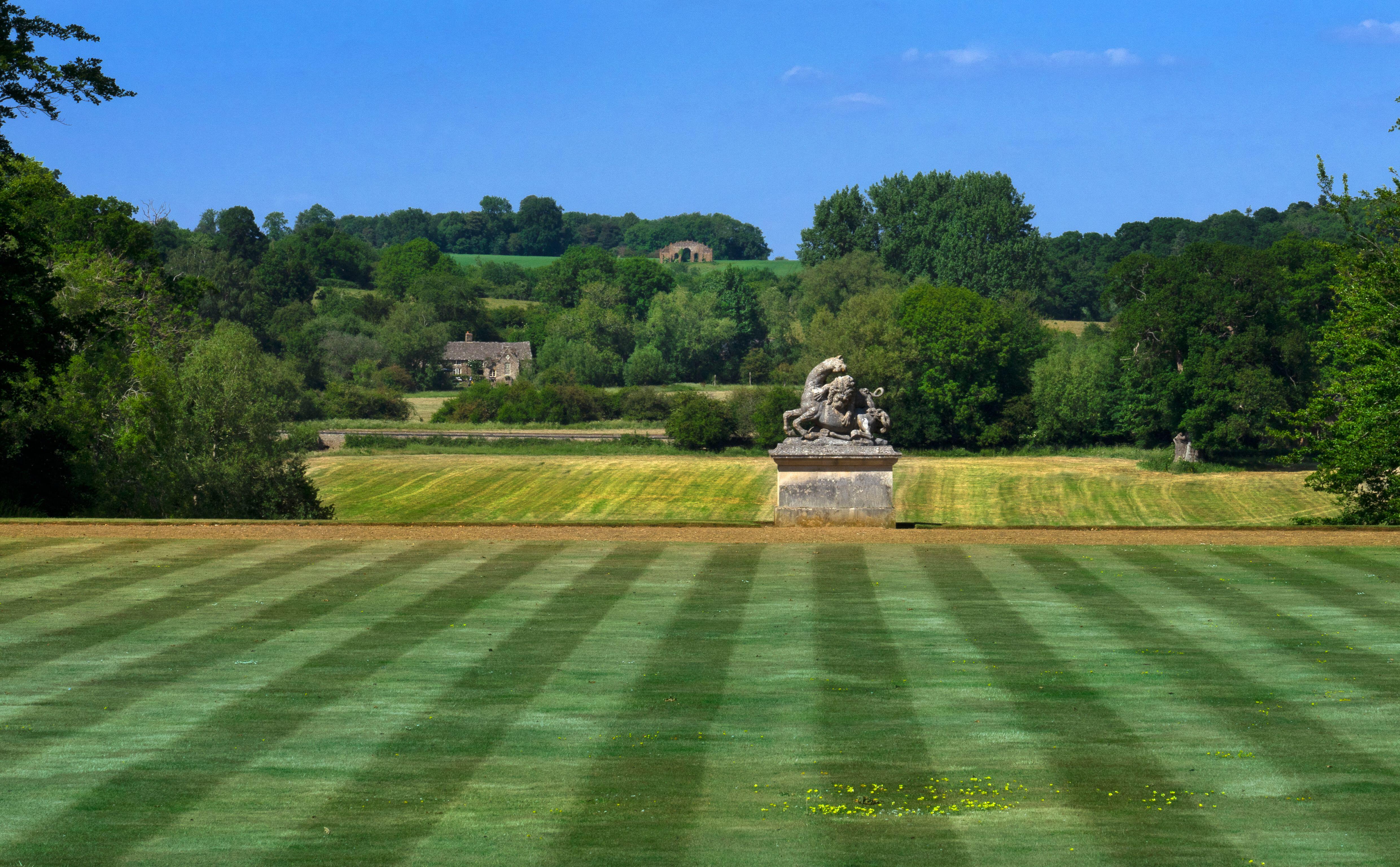 Main lawn at Rousham House and Gardens, with a sculpture of two horses and lions in the middle ground, and a small house and an old stone folly on a distant hillside.