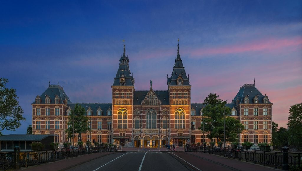 a large Gothic Revival building seen head on in an urban setting, the sky is dark blue of sunset streaked with pink