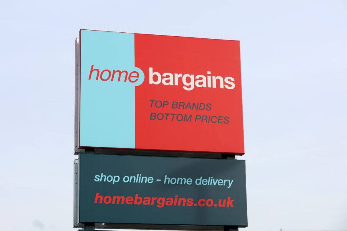 A large billboard with a blue and red background displays the text "home bargains" prominently. Below the main text, additional information is presented in smaller font, indicating services such as "Shop online" and "Furniture delivery." The billboard is set against a clear sky, enhancing the visibility of its message.