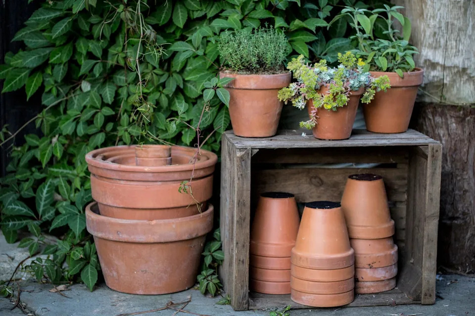 close up of stacks of terracotta flower pots on a stone floor and wooden box.