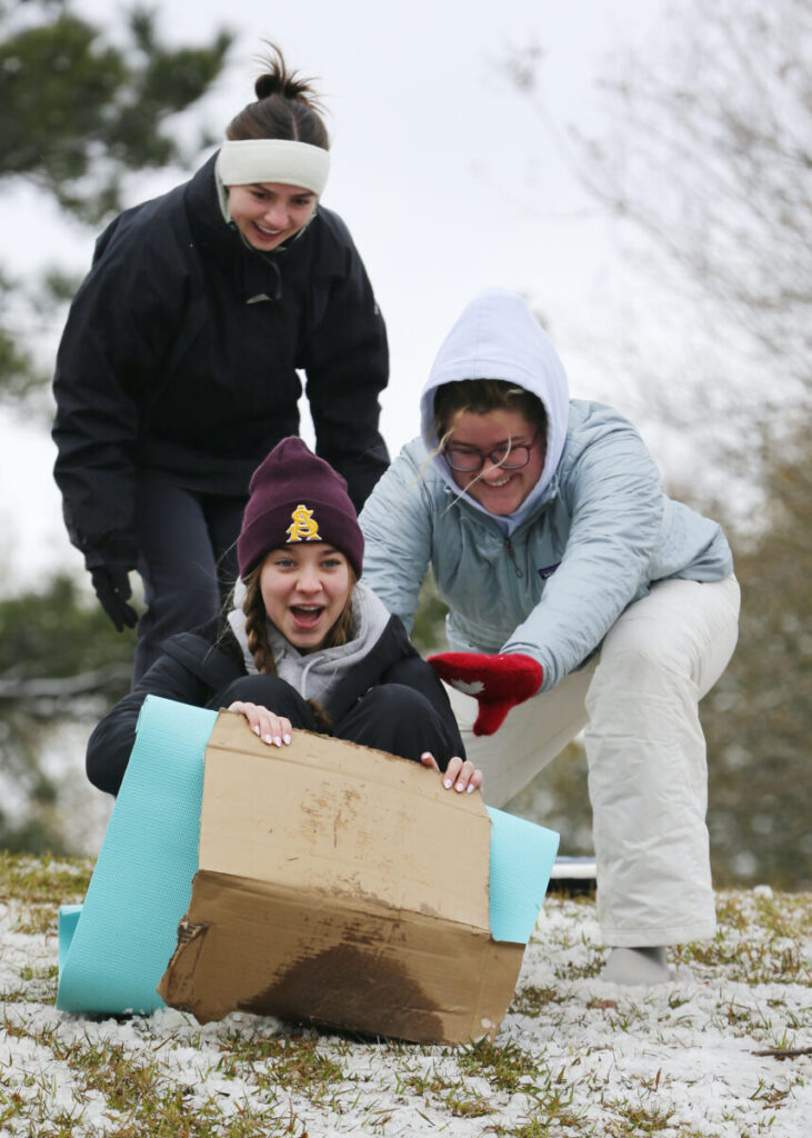 People sled down a snowy hill on a cardboard box