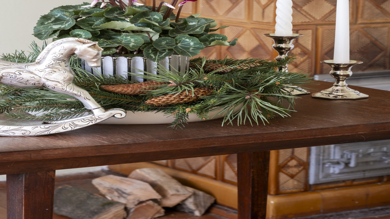 Potted cyclamen plant with holiday décor and two tall candlesticks in holders on a table.
