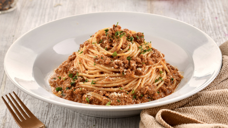 Spaghetti Bolognese served in a white dish with a fork and napkin aside it