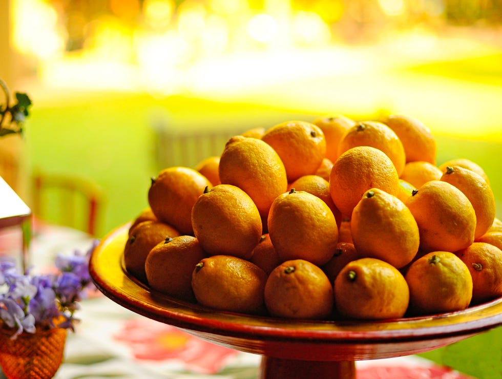 Close-up of a red serving dish displaying dozens of yellow lemons. Faded yellow background. the lemon is a popular citrus fruit, widely used in cooking for seasoning and in beverages. it is rich in vitamin c, which benefits the immune system, and also has antioxidant, anti inflammatory, and antibacterial properties. the fruit is cultivated worldwide, with brazil being one of the largest producers and exporters.