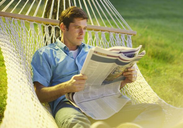 Man laying in hammock in garden, reading newspaper