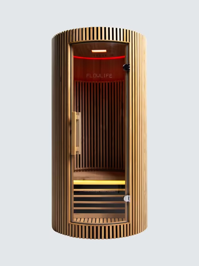 A cylindrical wooden sauna with vertical slats, a glass door, and red interior lighting.