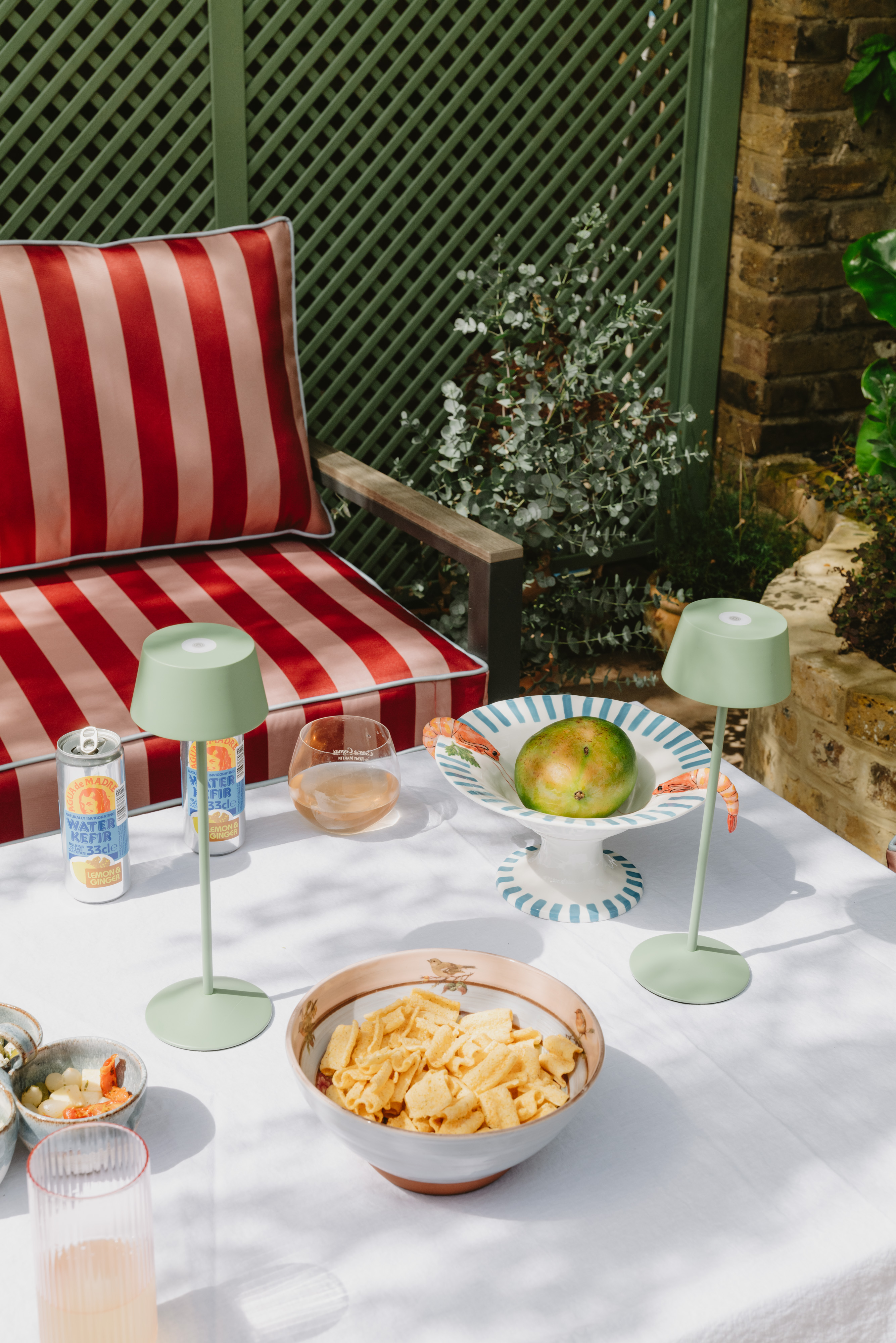 An outdoor table with snacks, drinks, and red and white striped cushions.