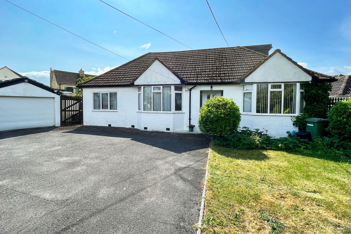 Stock photo showing close-up view of frontage of a whitewashed bungalow with bay windows with a tarmac driveway and parking garage.