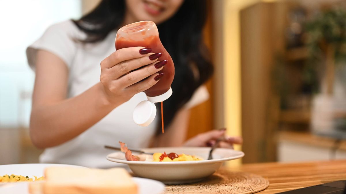 Cropped shot of young woman squeezing ketchup onto a breakfast dish consisting of toast. 
