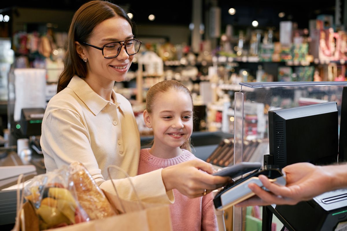 Portrait of woman with her child smiling while paying with smartphone at grocery store checkout smiling