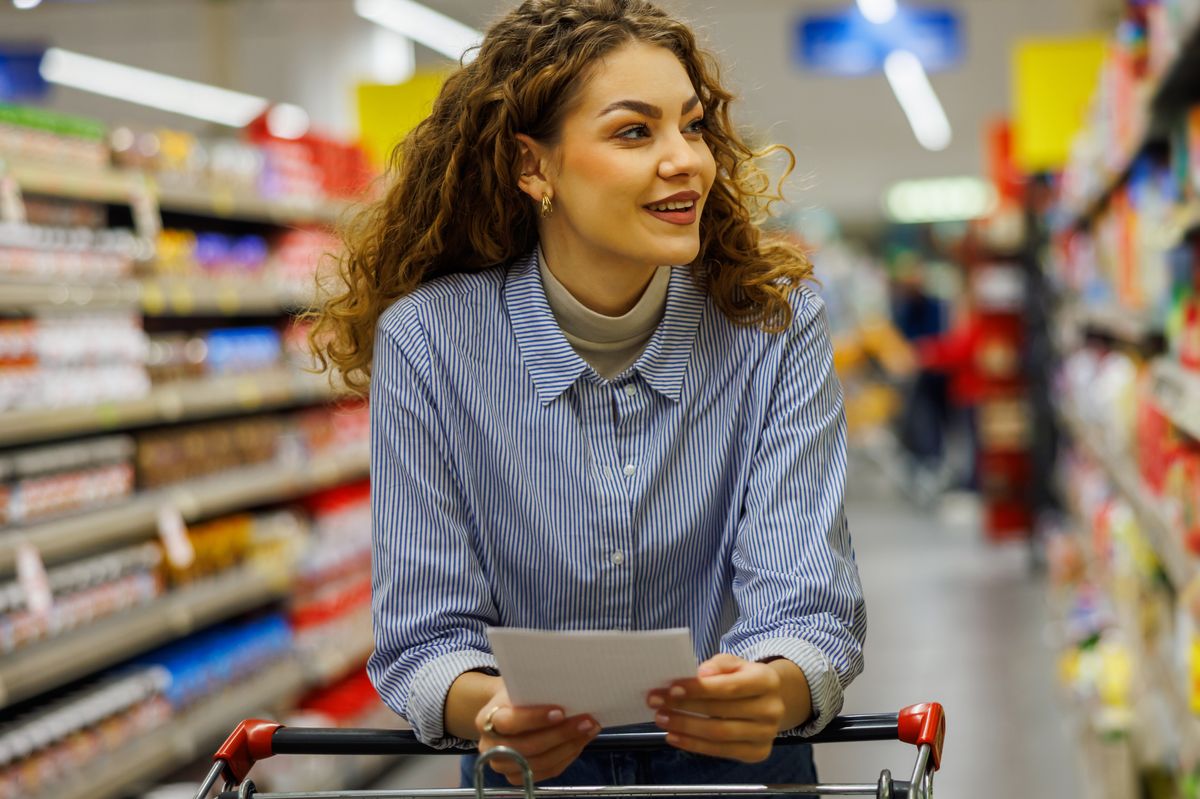 Beautiful young woman with curli hair shopping groceries in big and modern supermarket