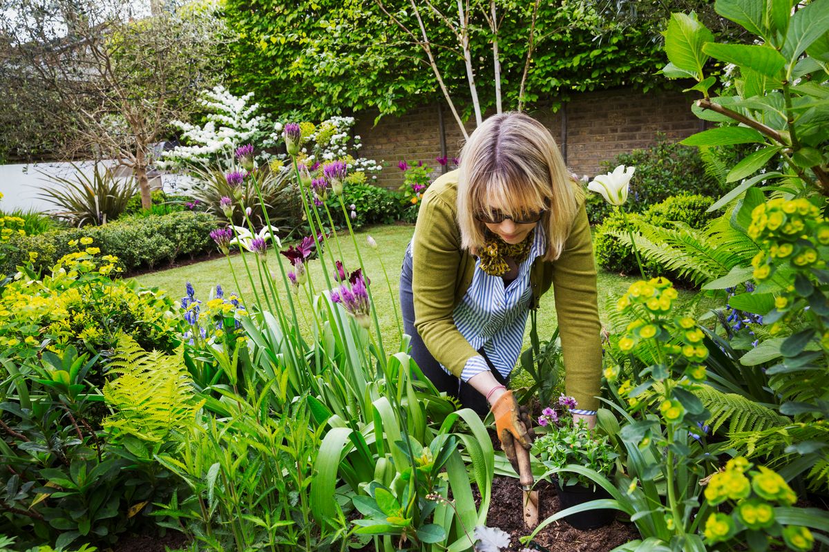Woman standing in a garden, holding a gardening trowel
