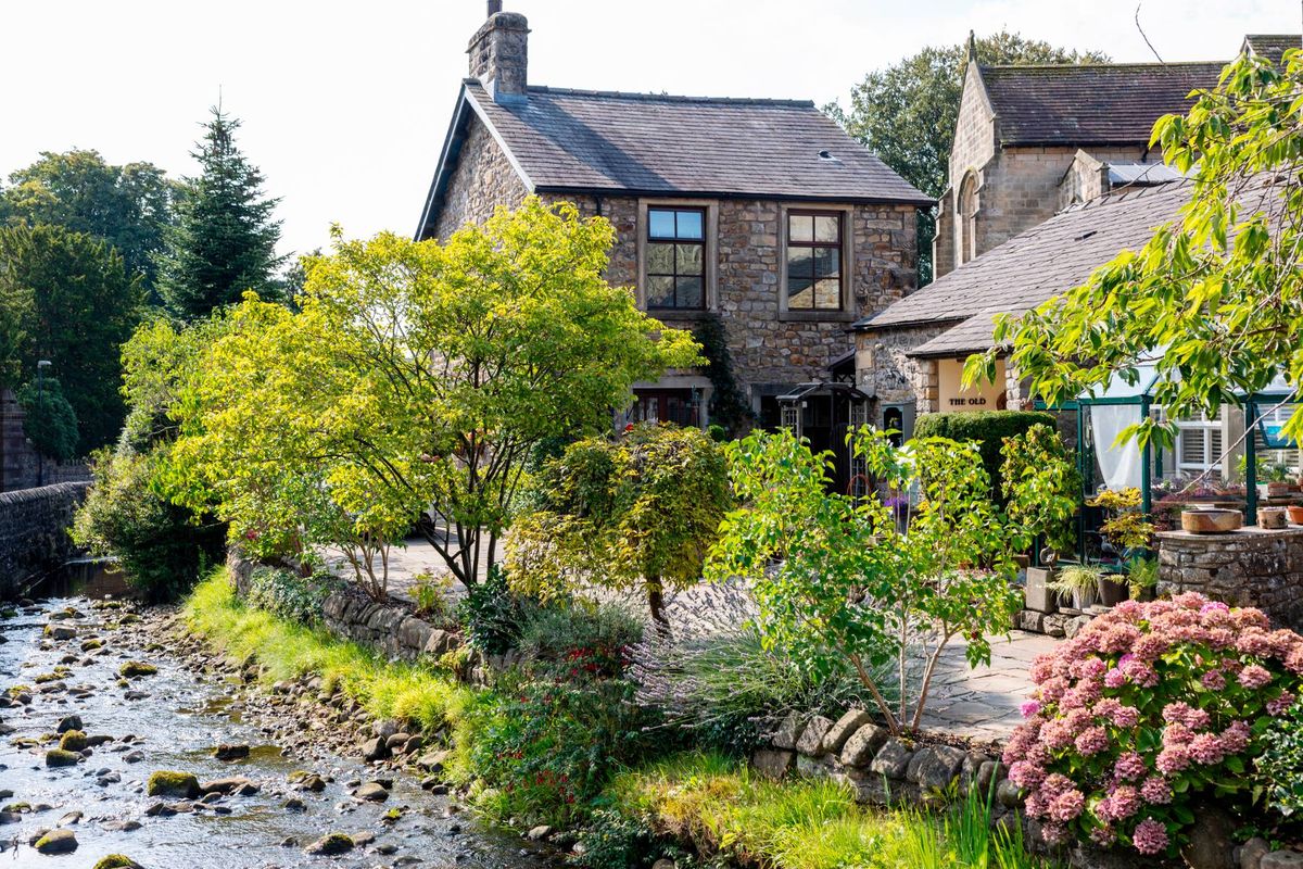 An aerial view of a residential property situated along a riverbank, surrounded by lush greenery and blooming flowers.