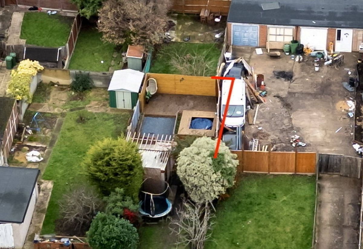 An aerial view of a residential property featuring a backyard with a pool, a wooden fence, and a red construction crane positioned at the center, indicating ongoing landscaping or construction work.