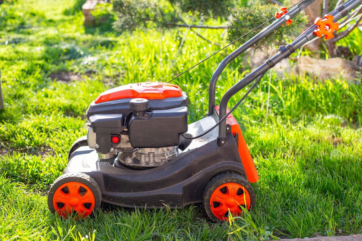 An orange and black lawn mower sits on a lush green lawn in the bright sun, ready to mow the grass