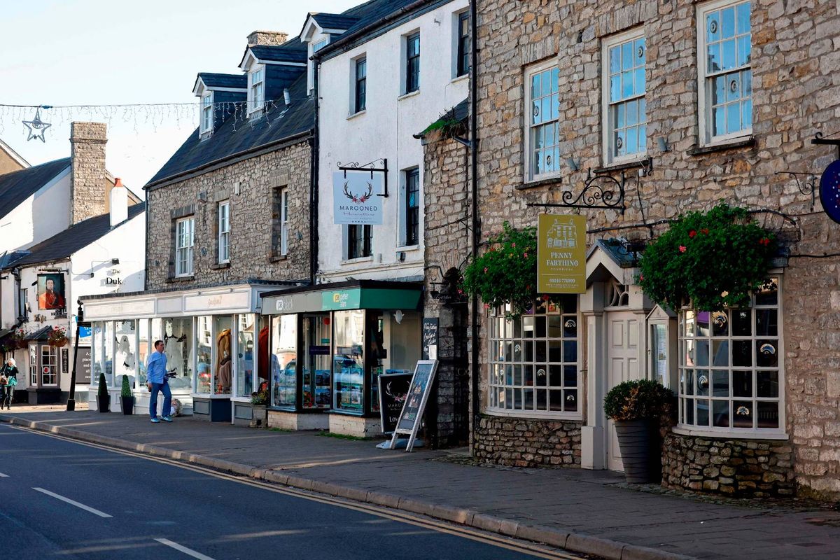 An image depicting a quaint street lined with traditional buildings featuring brick and stone facades, adorned with numerous windows and various awnings. The street is devoid of vehicles and pedestrians, presenting a serene and orderly urban landscape.