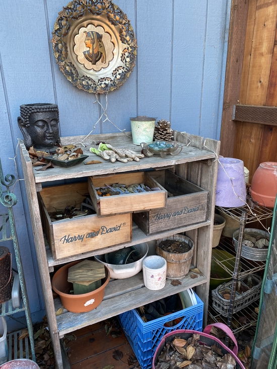 wooden bookshelf and metal rack in the corner of the p;atio loaded with empty pots and various other garden supplies.