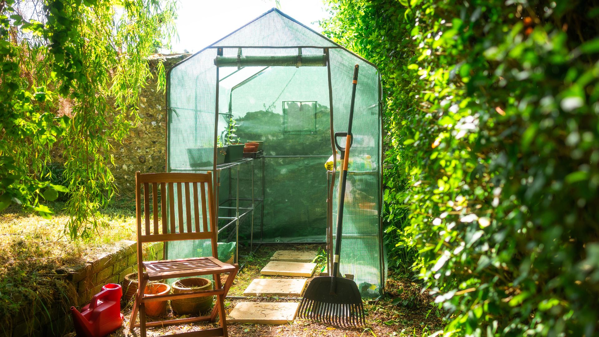 picture of greenhouse with rake and chair outside it