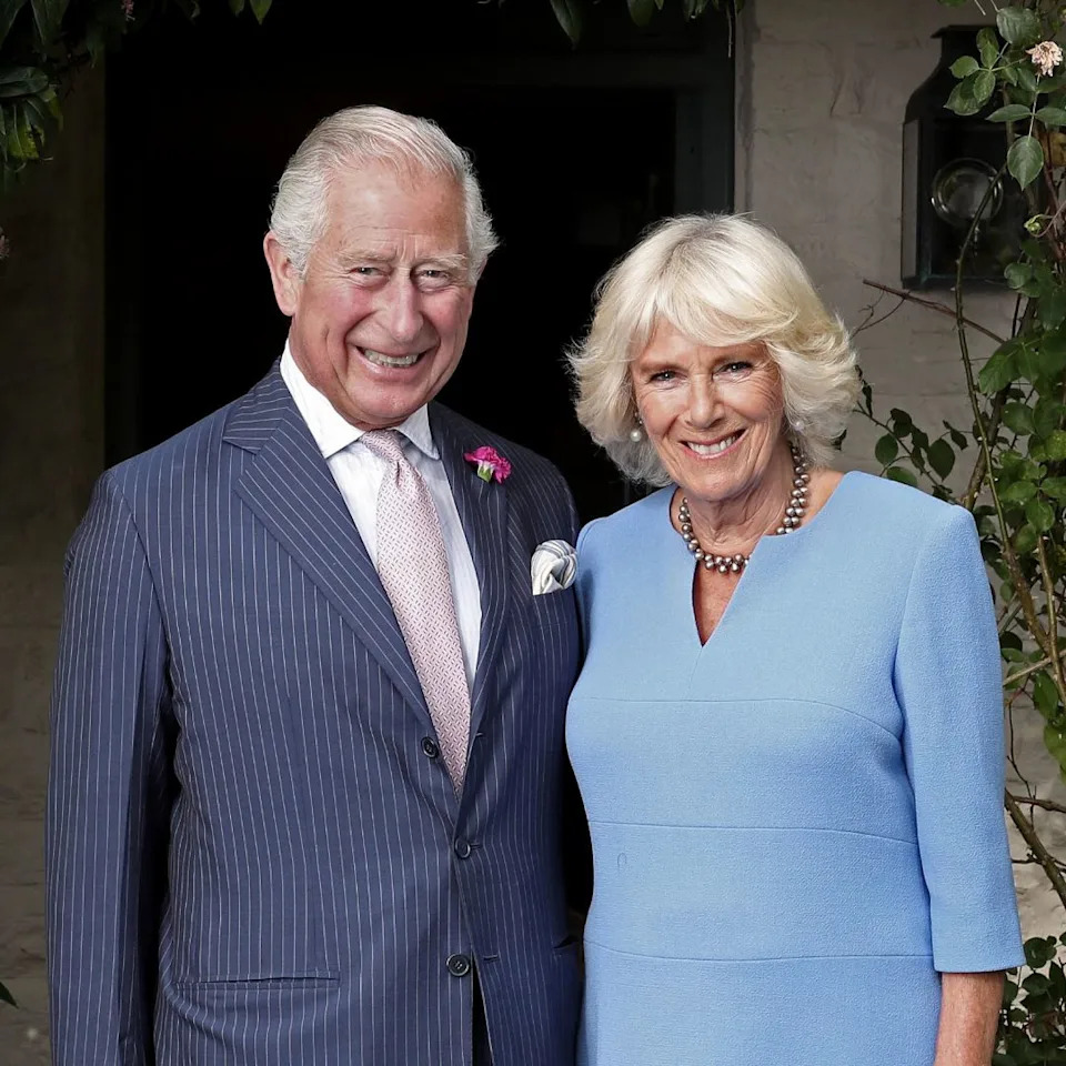 King Charles in a striped blue suit standing next to Queen Camilla, in a blue dress, and smiling .